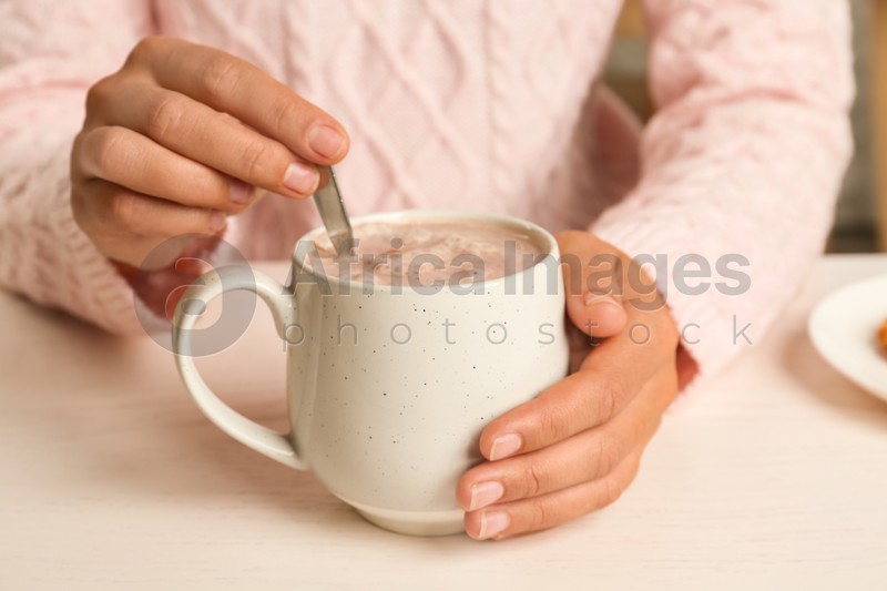 Woman holding cup of delicious cocoa drink at white table, closeup