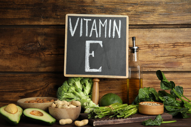 Small chalkboard with phrase Vitamin E and different products on wooden background