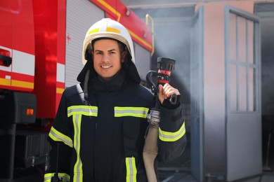 Portrait of firefighter in uniform with high pressure water jet near fire truck outdoors