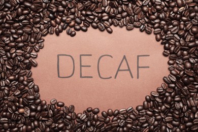 Word Decaf and coffee beans on brown background, top view