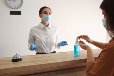 Woman applying antiseptic gel at hotel reception, closeup