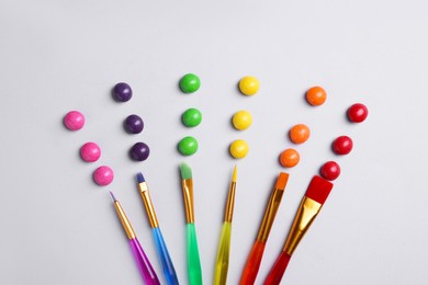 Creative flat lay composition with paint brushes and colorful candies on light grey background