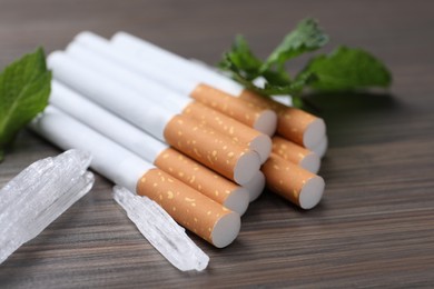 Cigarettes, menthol crystals and mint on wooden table, closeup