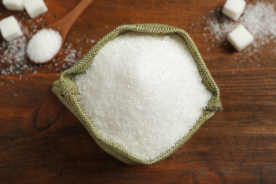 Photo of Granulated sugar in sack on wooden table, flat lay
