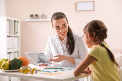Professional nutritionist with tablet consulting little girl in office