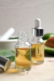 Bottle of essential oil, pipette and fresh avocado on table, closeup