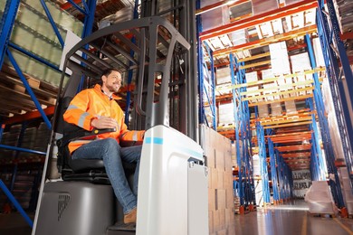 Happy worker sitting in forklift truck at warehouse, low angle view