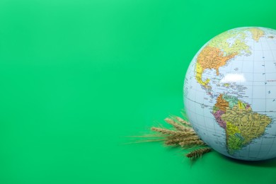 Globe with wheat spikelets on green background, space for text. Hunger crisis concept