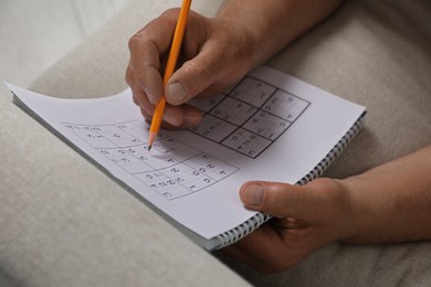 Senior man solving sudoku puzzle on sofa at home, closeup