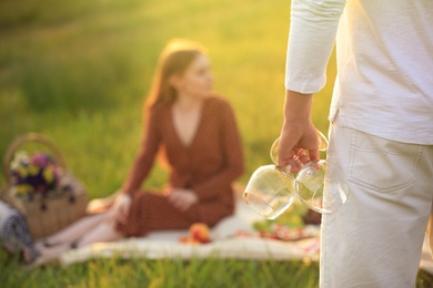 Photo of Young man with wineglasses and blurred woman on background outdoors, closeup. Picnic season