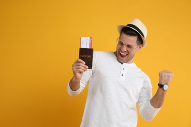 Excited male tourist holding passport with ticket on yellow background, space for text
