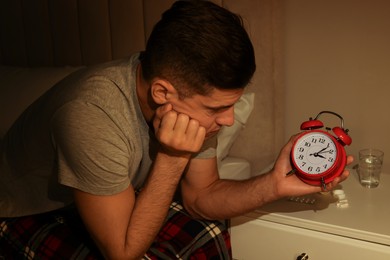 Man suffering from insomnia looking at time on alarm clock in bedroom