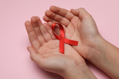 Little girl holding red ribbon on pink background, closeup. AIDS disease awareness