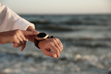 Young woman checking smart watch on beach at sunset, closeup