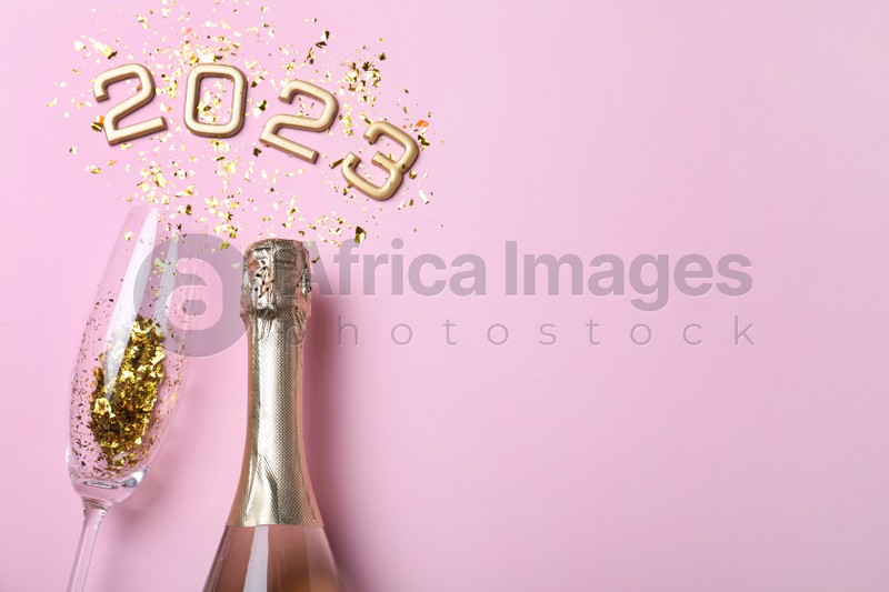 Bottle of sparkling wine, glass, golden confetti and number 2023 on pink background, flat lay with space for text. Happy New Year