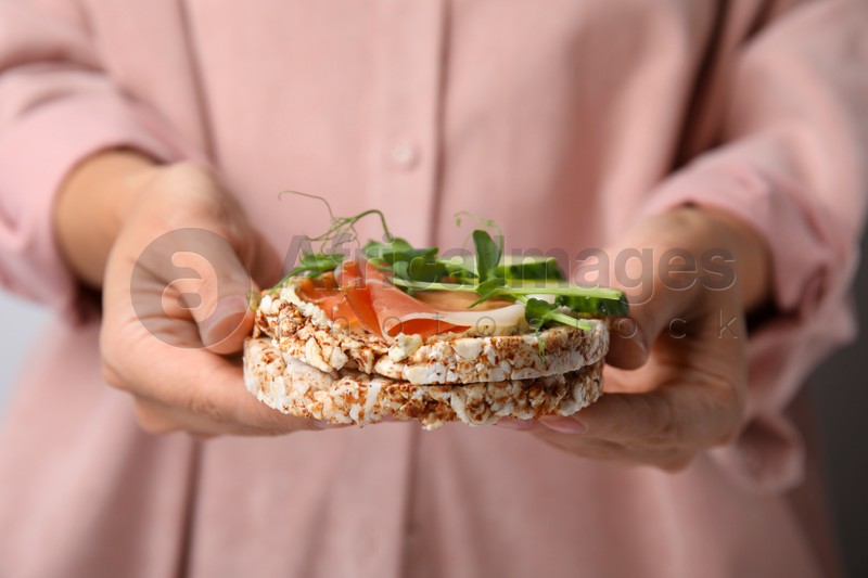 Woman holding crunchy buckwheat cakes with prosciutto, microgreens and cucumber, closeup