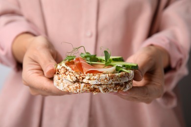 Woman holding crunchy buckwheat cakes with prosciutto, microgreens and cucumber, closeup