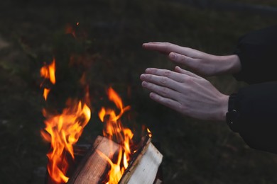 Tourist warming hands near bonfire outdoors in evening, closeup