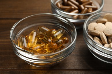 Photo of Different dietary supplements in glass bowls on wooden table, closeup