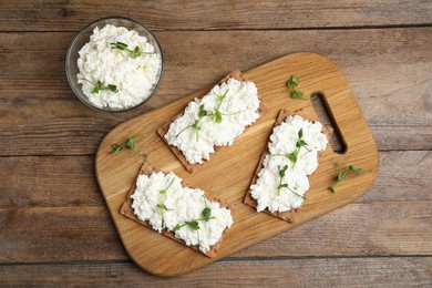 Photo of Crispy crackers with cottage cheese and microgreens on wooden table, flat lay