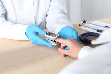 Photo of Doctor examining patient with modern fingertip pulse oximeter at wooden table, closeup