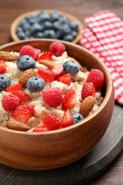Tasty oatmeal porridge with berries and almond nuts in bowl served on table, closeup