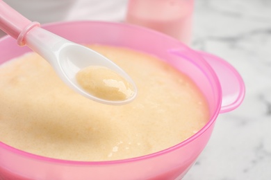 Spoon of healthy baby food over bowl on table, closeup