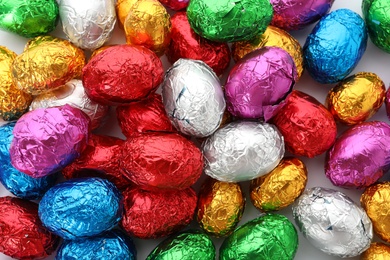 Many chocolate eggs wrapped in bright foil as background, top view