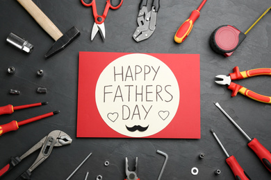Card with phrase HAPPY FATHER'S DAY and different tools on stone background, flat lay