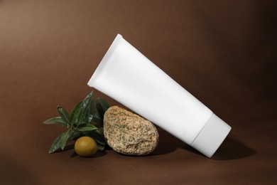 Photo of Tube of natural cream, stone and olive on brown background. Cosmetic products