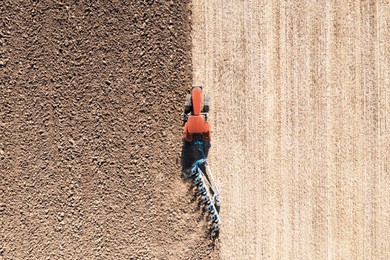 Tractor pulling plow in agricultural field on sunny day, aerial view