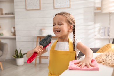 Photo of Cute little girl with brush and rag singing while cleaning at home