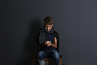Poor boy with pieces of bread on dark background