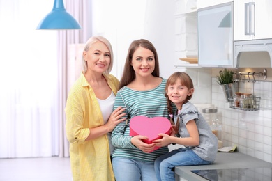 Beautiful mature lady, daughter and grandchild with gift box in kitchen. Happy Women's Day