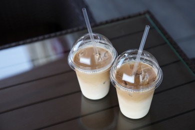 Photo of Plastic takeaway cups of delicious iced coffee on table in outdoor cafe, space for text
