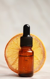 Bottle of organic cosmetic product and dried orange slice on light marbled background, closeup
