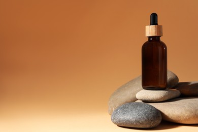 Photo of Bottle of face serum and spa stones on beige background, space for text