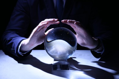 Businessman using crystal ball to predict future at table in darkness, closeup