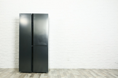 Modern refrigerator near white brick wall, space for text