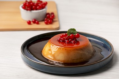 Photo of Plate of delicious caramel pudding with red currants and mint on white wooden table