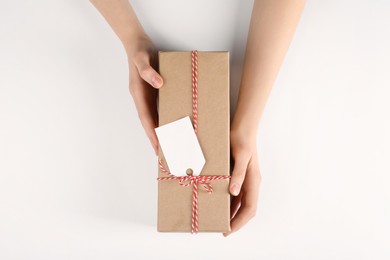 Woman holding parcel wrapped in kraft paper with tag on white background, top view
