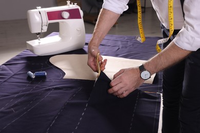 Professional tailor cutting fabric by following chalked sewing pattern at table in workshop, closeup