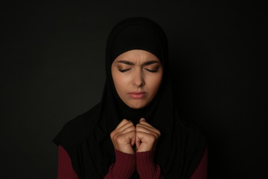 Portrait of sad Muslim woman in hijab  praying on dark background