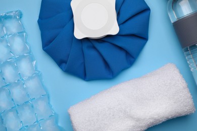 Bottle of water, cold compress, ice pack and towel on light blue background, flat lay. Heat stroke treatment