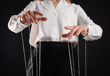 Woman in formal outfit pulling strings of puppet on black background, closeup