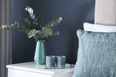 Photo of Beautiful eucalyptus branches and candles on nightstand in bedroom. Interior element