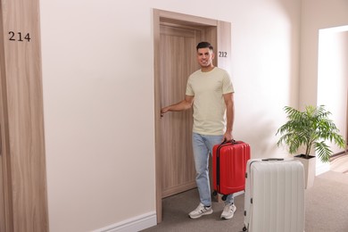 Happy man with suitcase opening door in hotel