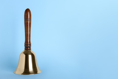 Golden school bell with wooden handle on light blue background. Space for text