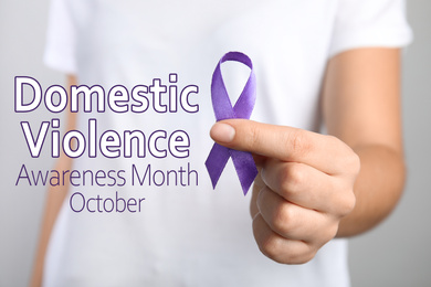 Woman holding purple ribbon on grey background, closeup. Symbol of Domestic Violence Awareness
