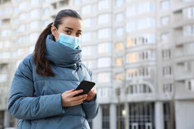 Woman with disposable mask and smartphone outdoors. Dangerous virus